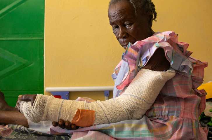 A Haitian woman looks at her arm, which is wrapped in a bandage.