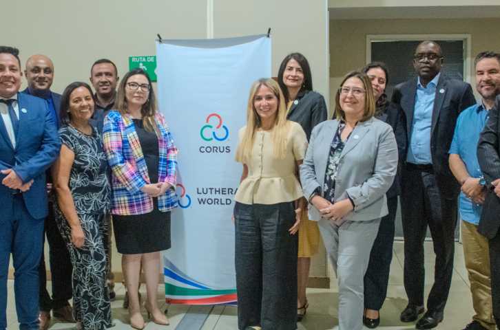 A group of Corus team members stands in front of a Corus banner
