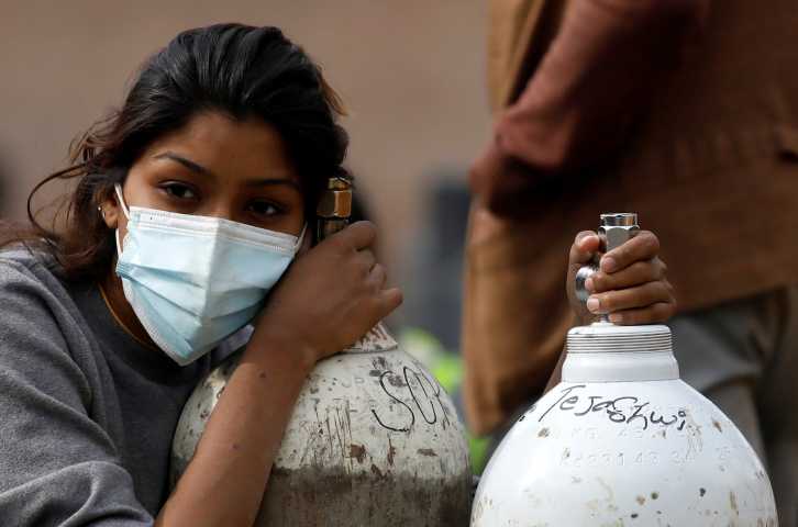 A woman wearing a face is leaning on an oxygen tank.